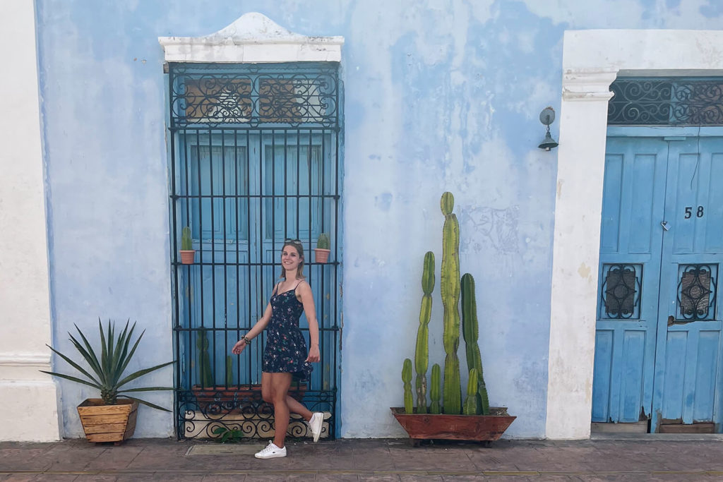 Frau läuft vor einer blauen Wand mit Türen und Pflanzen